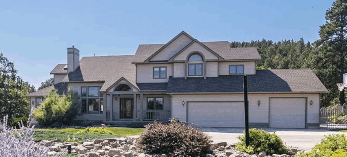 Exterior view of a large custom home remodeled by JG Carpentry, featuring updated roofing, windows, and siding as part of a full-service whole-home renovation surrounded by landscaped greenery.