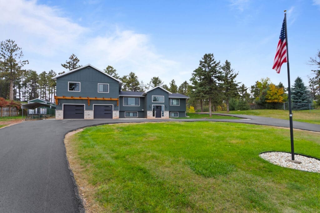 Full-home addition and remodel in Rapid City, SD by JG Carpentry with blue-gray board-and-batten siding, stone accents and a cedar pergola over the garage.