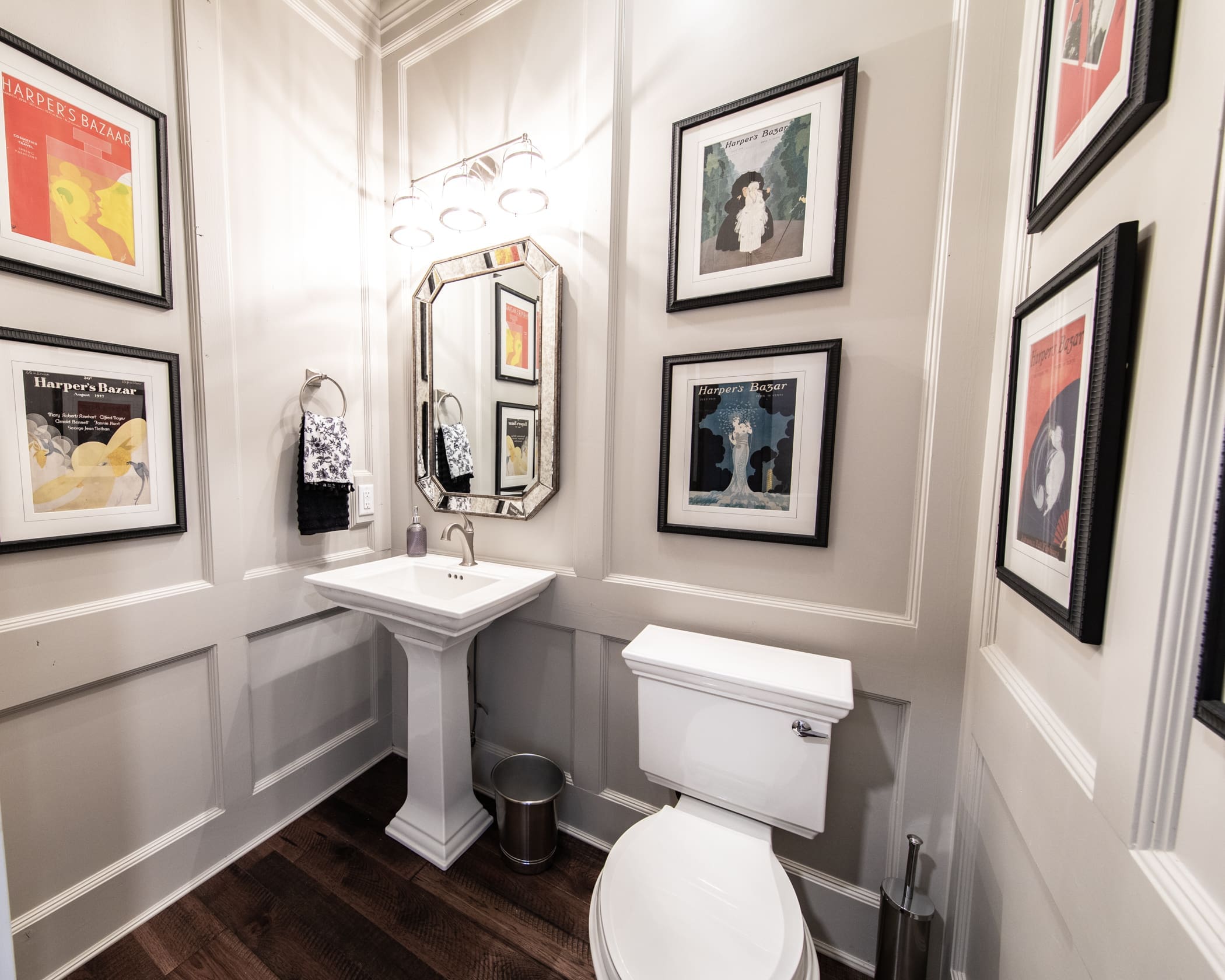 Elegant custom bathroom remodeled by JG Carpentry, featuring a pedestal sink, modern toilet, decorative wall paneling, hardwood flooring, and framed vintage magazine covers as wall art.