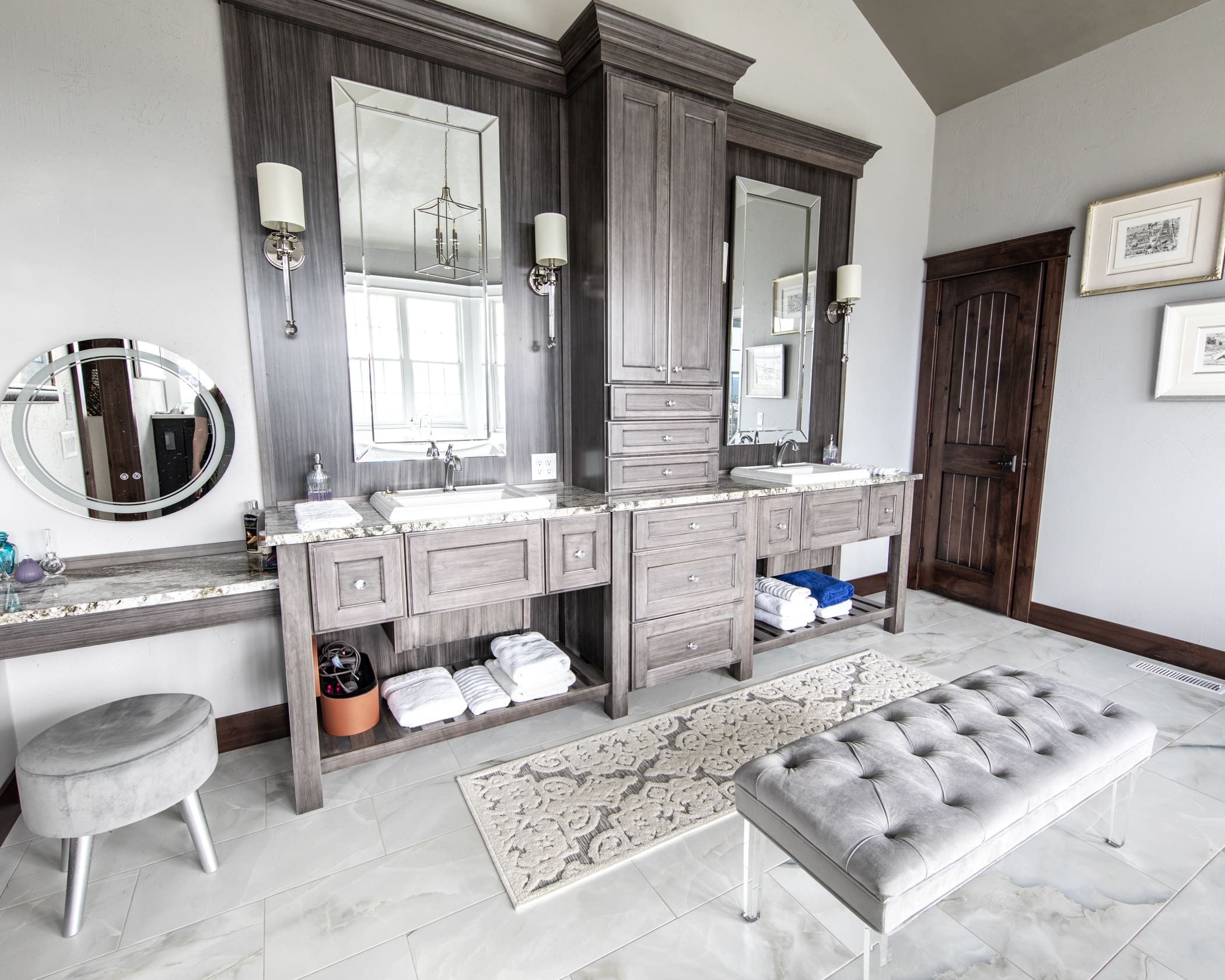 Custom bathroom remodel by JG Carpentry in Rapid City, SD featuring dual vanities with gray cabinetry, marble countertops, and a modern seating area.