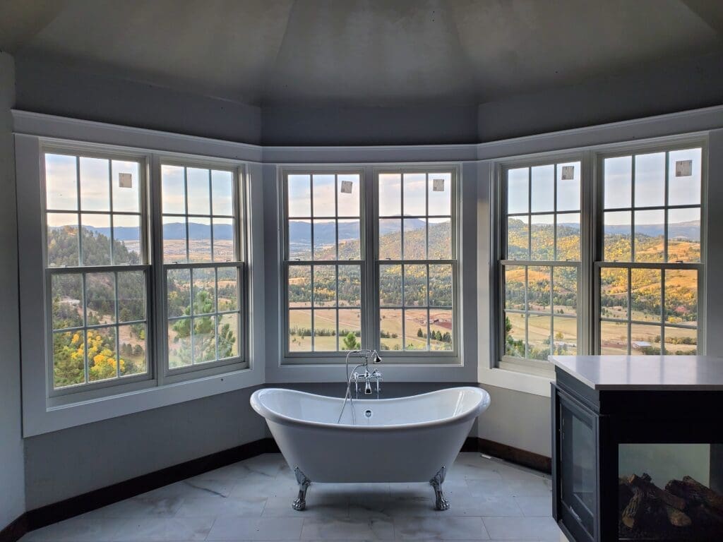 Finished bathroom remodel by JG Carpentry in Spearfish, SD, featuring a freestanding clawfoot tub positioned in front of large bay windows with panoramic views of rolling hills and autumn foliage, creating a serene and luxurious setting.